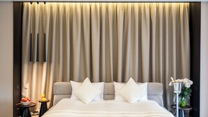 Een hotelkamer met een groot bed, een nachtkastje met een schaal fruit, een vaas met bloemen en een minibar.