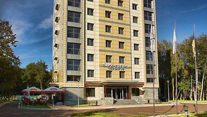 A multi-story hotel with a modern design, featuring a prominent entrance and a parking area in front.