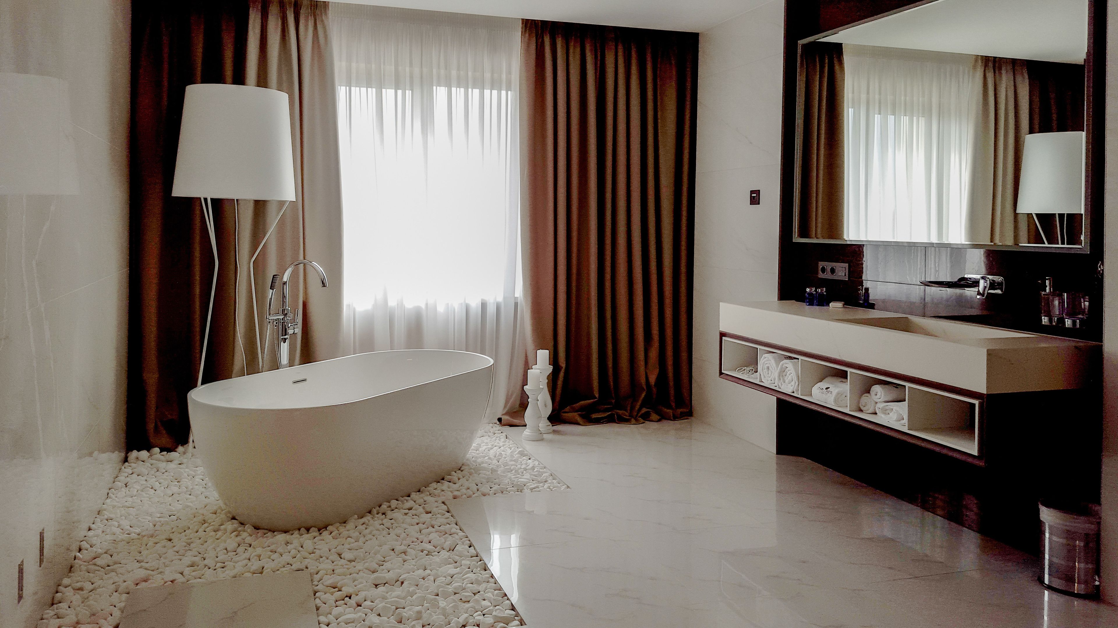 A modern bathroom with a freestanding bathtub, a vanity with a mirror, and a large window with curtains.