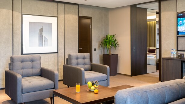 Een moderne hotel lobby met grijze bekleding, een bijzettafeltje met fruit, een lijst met een foto aan de muur en een televisie aan de rechterkant.