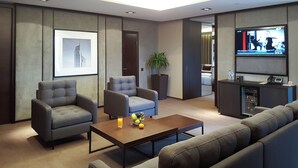 Een moderne woonkamer met een bank, fauteuils, een bijzettafel met fruit, een televisie en een plant.