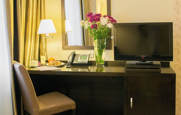 A hotel room desk with a television, phone, and a vase of flowers.