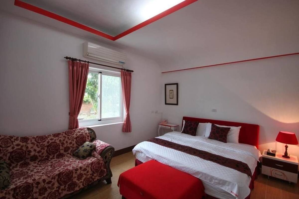A bedroom with a bed, a sofa, a nightstand, and a window with curtains.