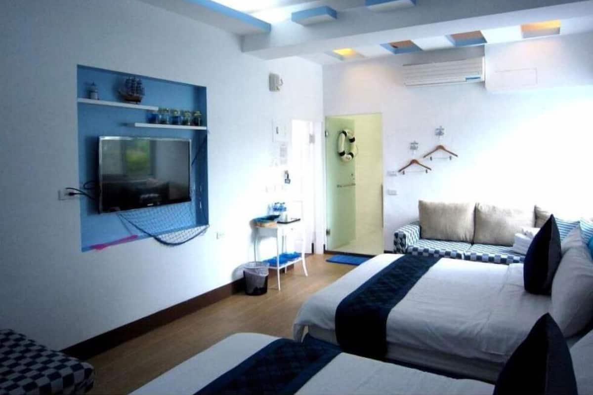 A hotel room with two beds, a TV mounted on the wall, a small table, and a door with a coat rack.