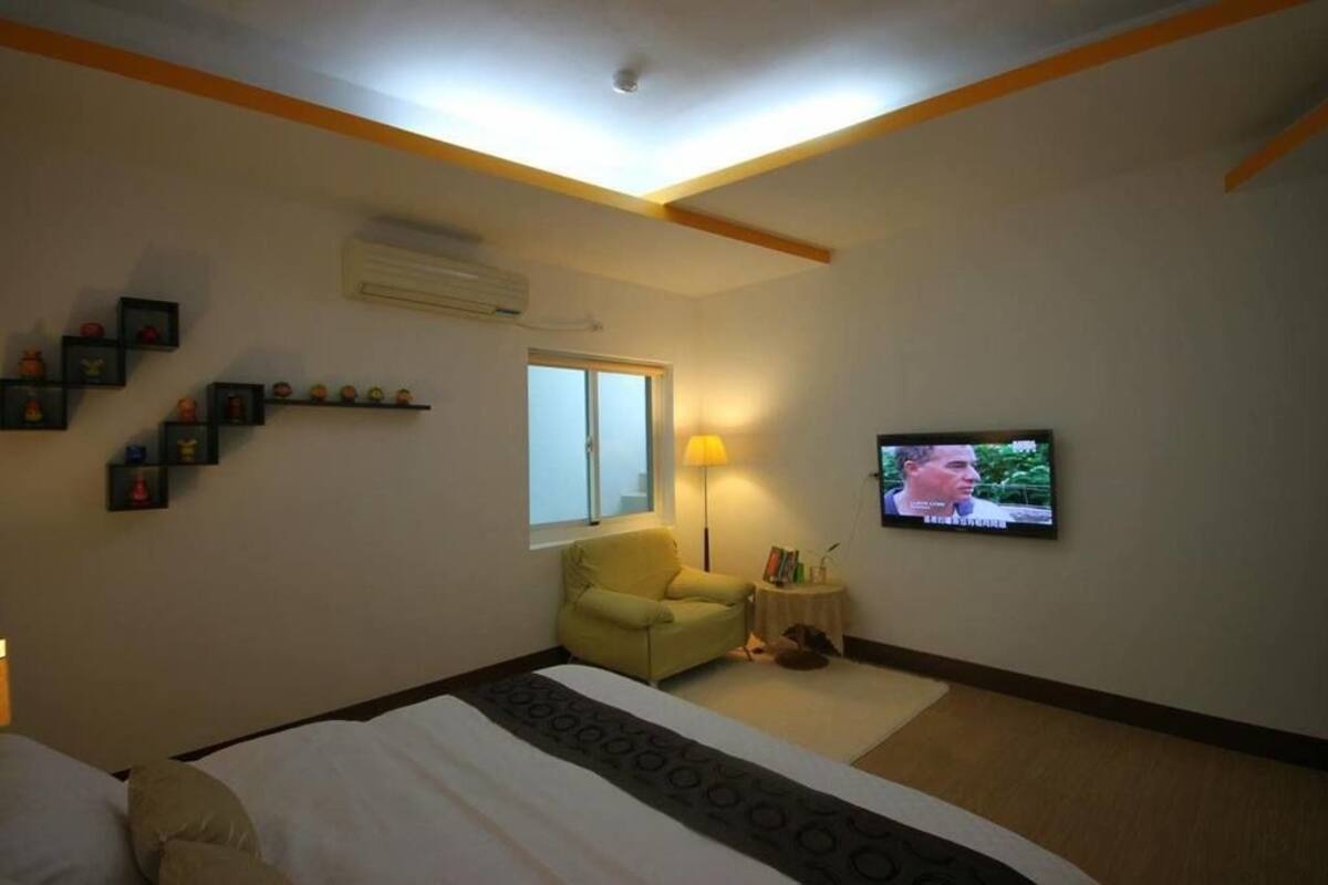 A hotel room with a bed, a chair, a TV, and a window.