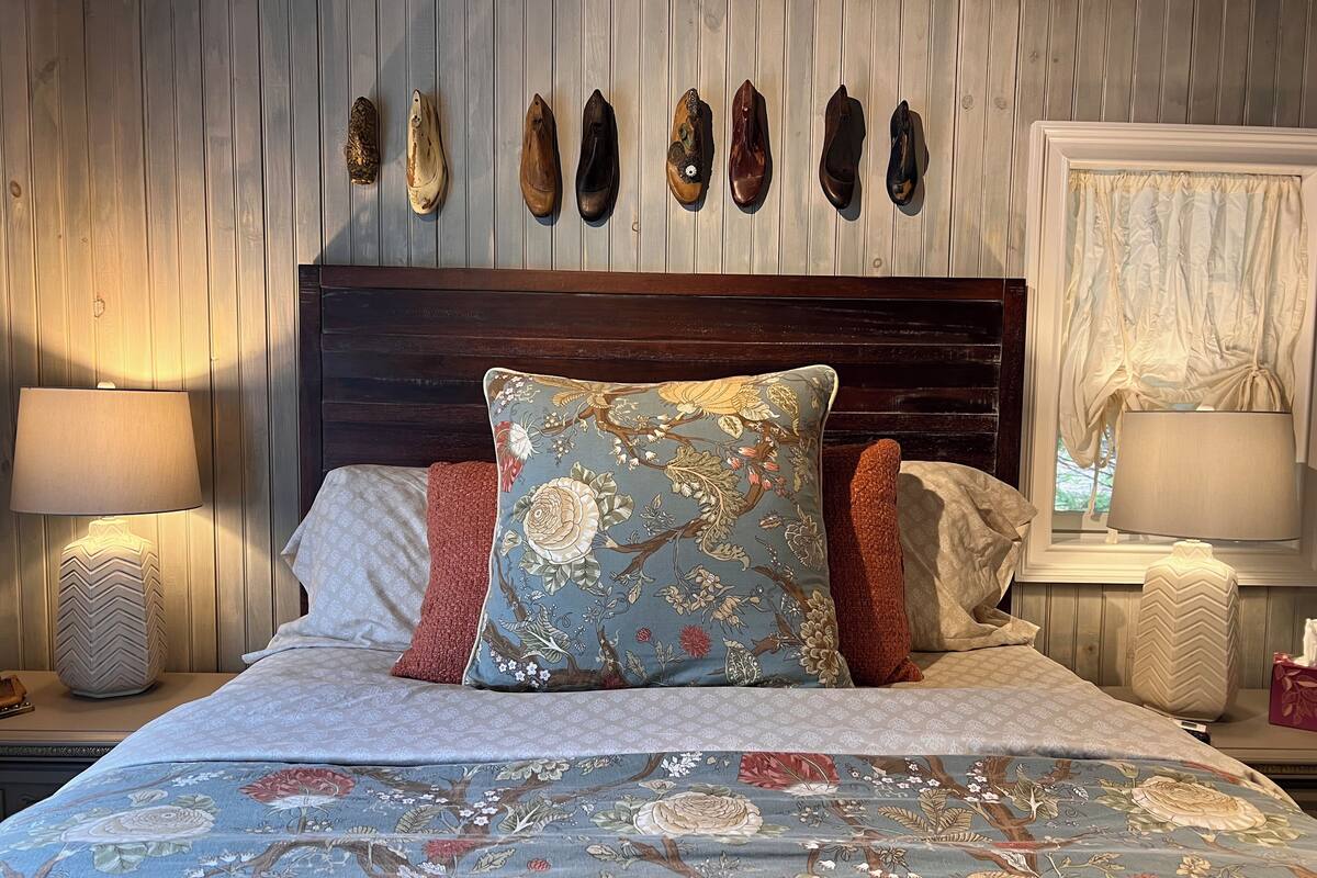 A bed with floral bedding, a decorative pillow, and a wall-mounted shoe rack.