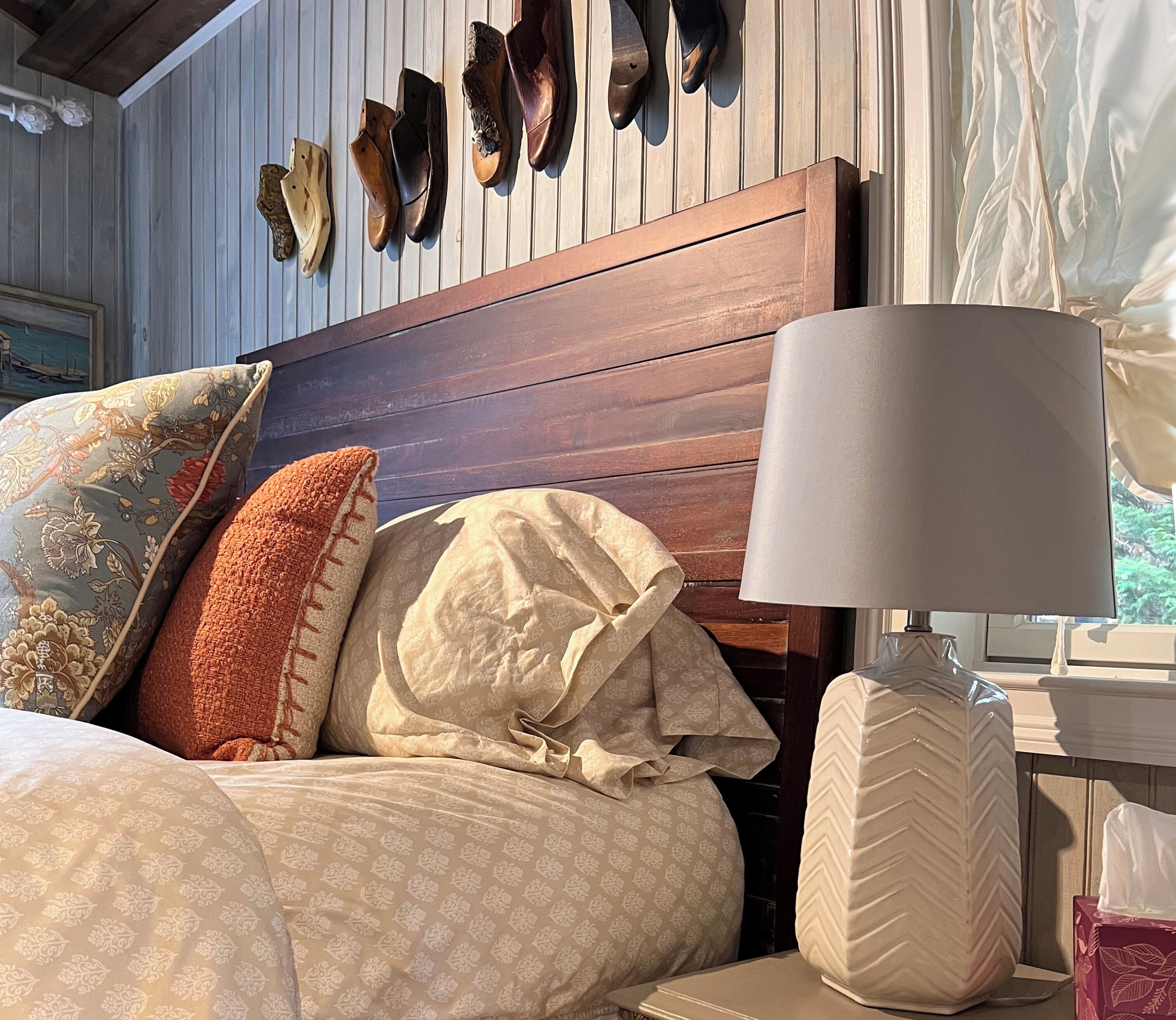 Una cama con varias almohadas, cabecero de madera y una lámpara de noche.