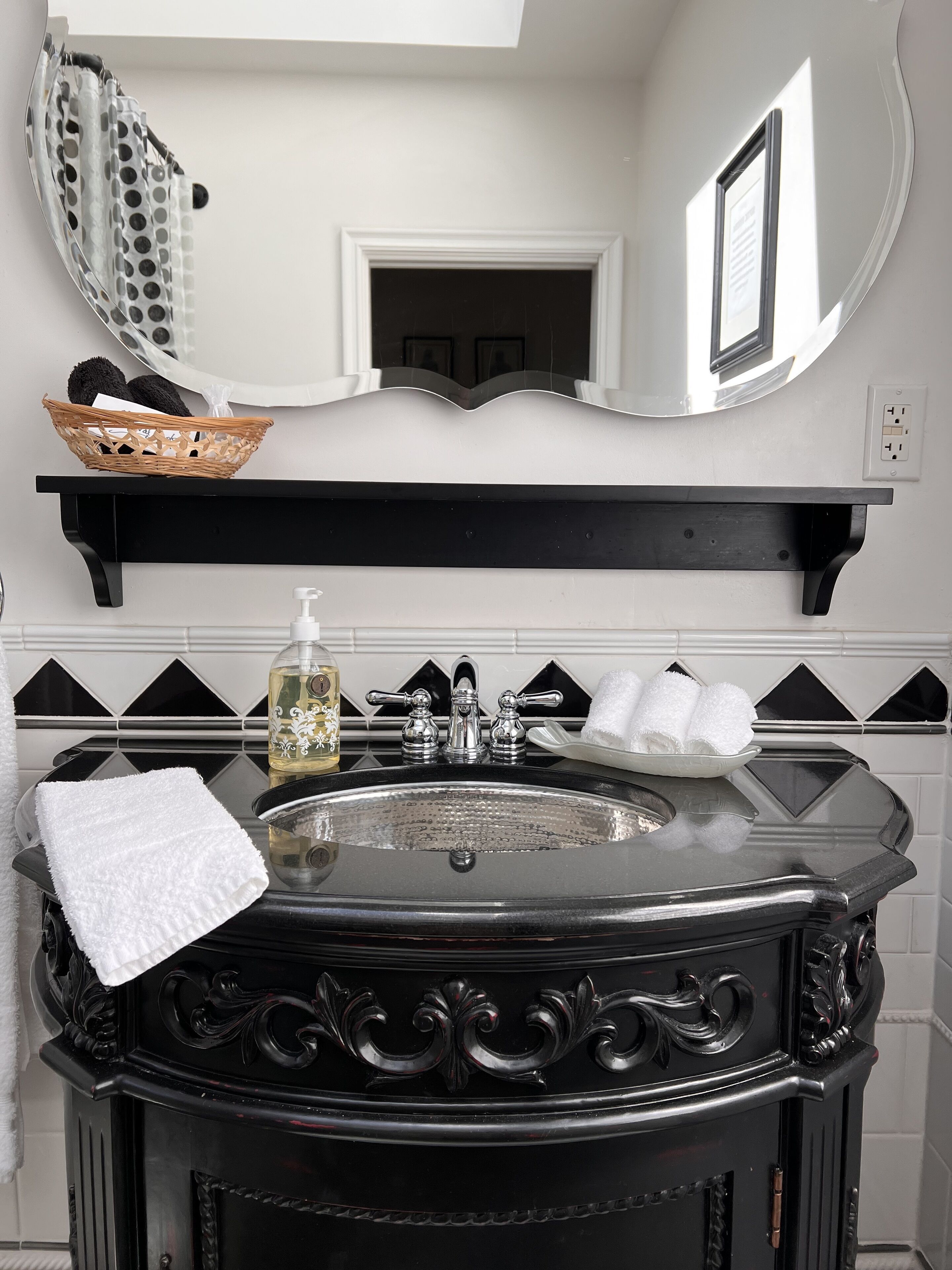 A bathroom with a black vanity, a mirror above the sink, a white towel, and a bottle of hand soap.