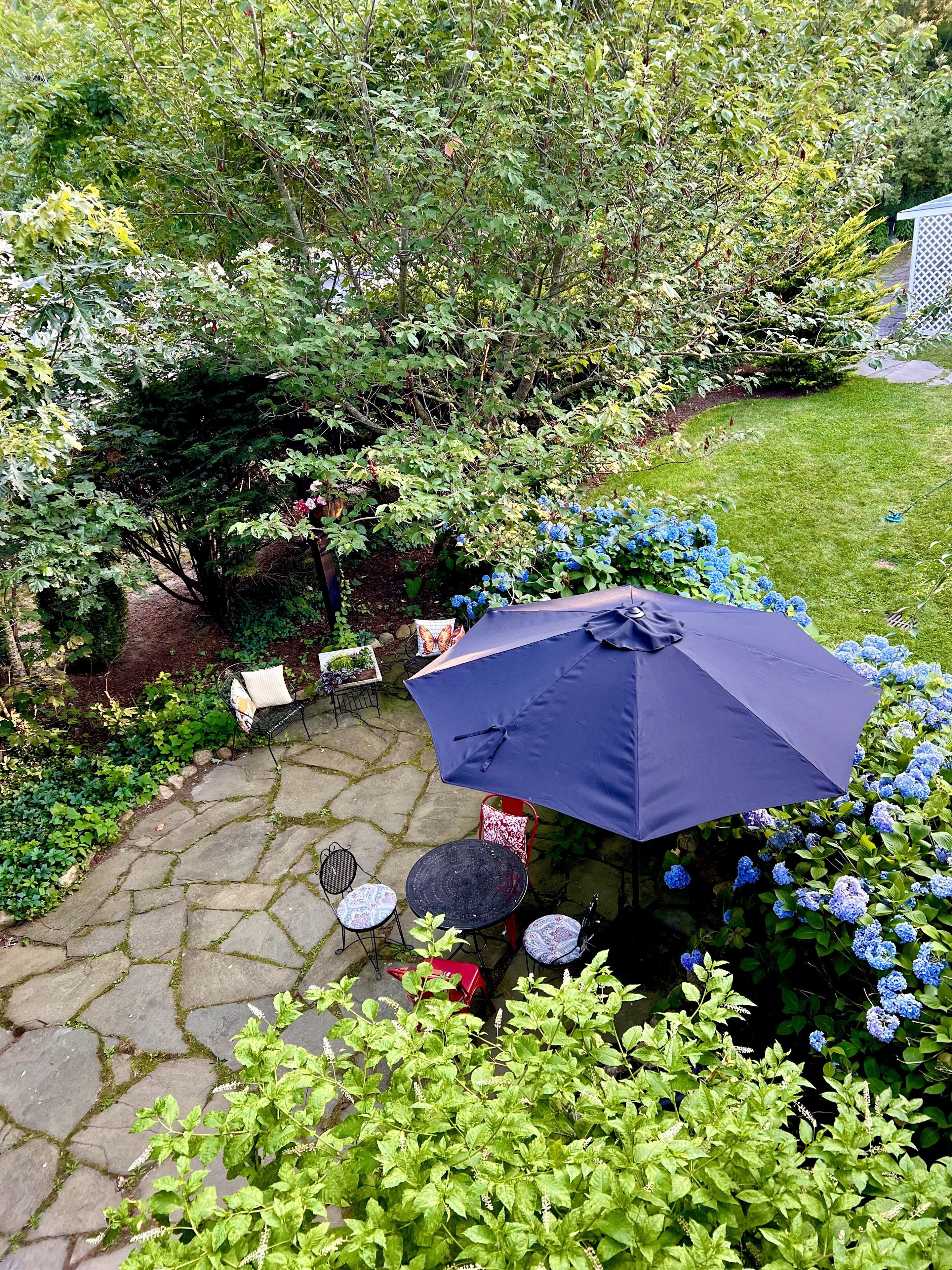 Eine Terrasse mit Steinböden, Gartenmöbeln und einem großen Sonnenschirm.