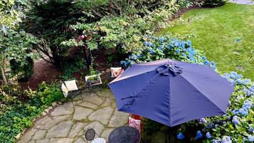 Eine Terrasse mit Steinböden, Gartenmöbeln und einem großen Sonnenschirm.