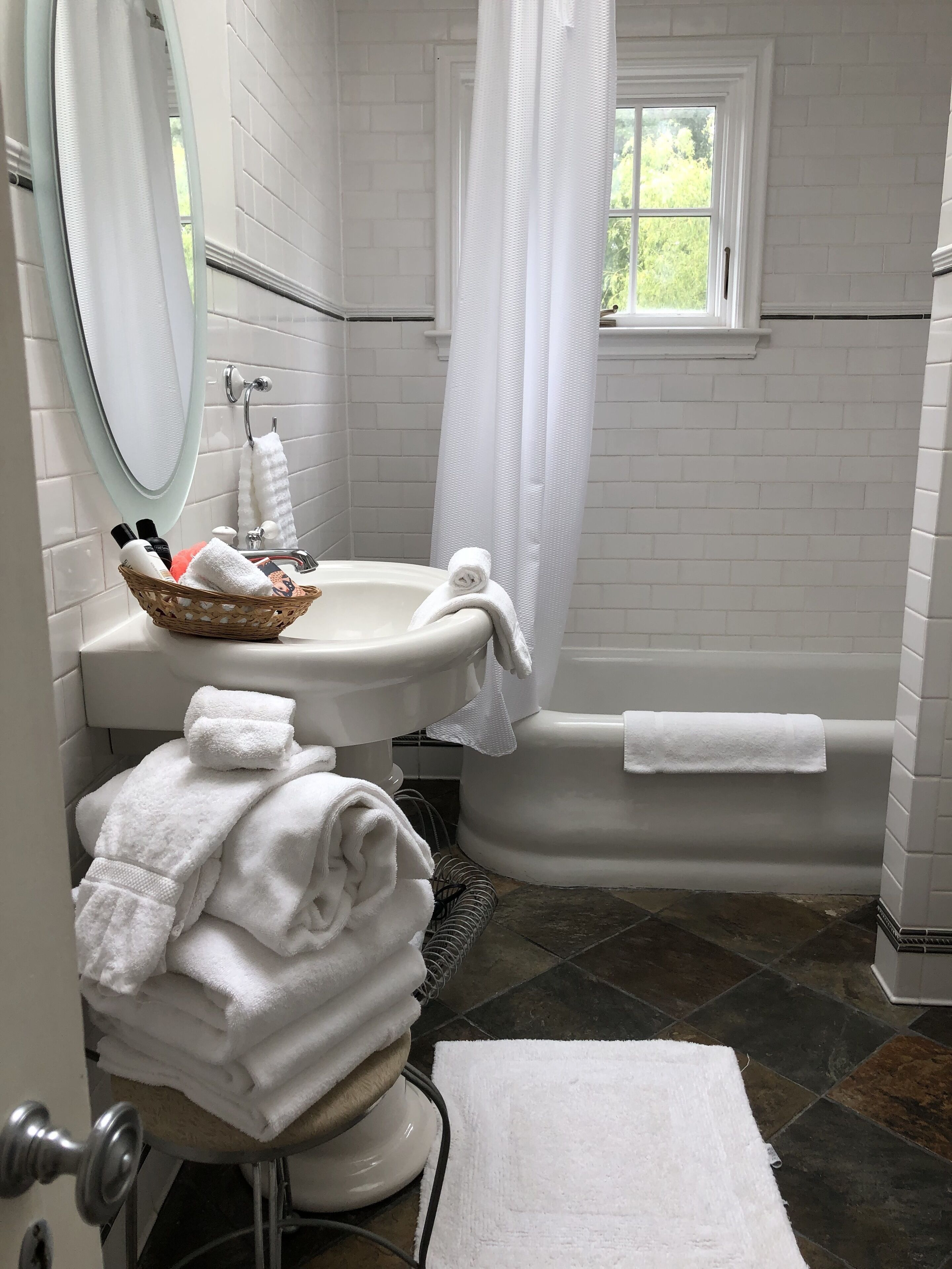 A bathroom with a white bathtub, a sink, and a mirror. There are towels and toiletries on the sink.