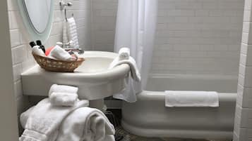 A bathroom with a white bathtub, a sink, and a mirror. There are towels and toiletries on the sink.