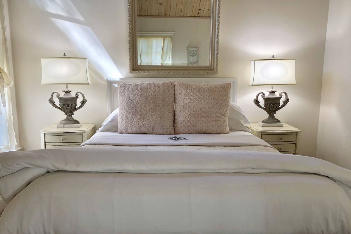 A neatly made bed with two fluffy pillows, two bedside tables with lamps, and a large mirror above the bed.