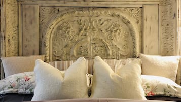 A bed with a headboard featuring intricate carvings, a floral-patterned pillow, and a brown bedspread.