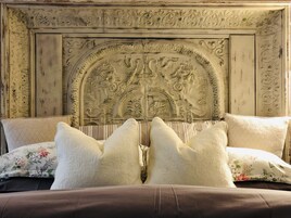 A bed with a headboard featuring intricate carvings, a floral-patterned pillow, and a brown bedspread.