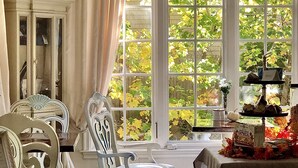 A room with a large window, a dining table with a tablecloth, and a chair with a cushion. - Frederick William House (Falmouth)