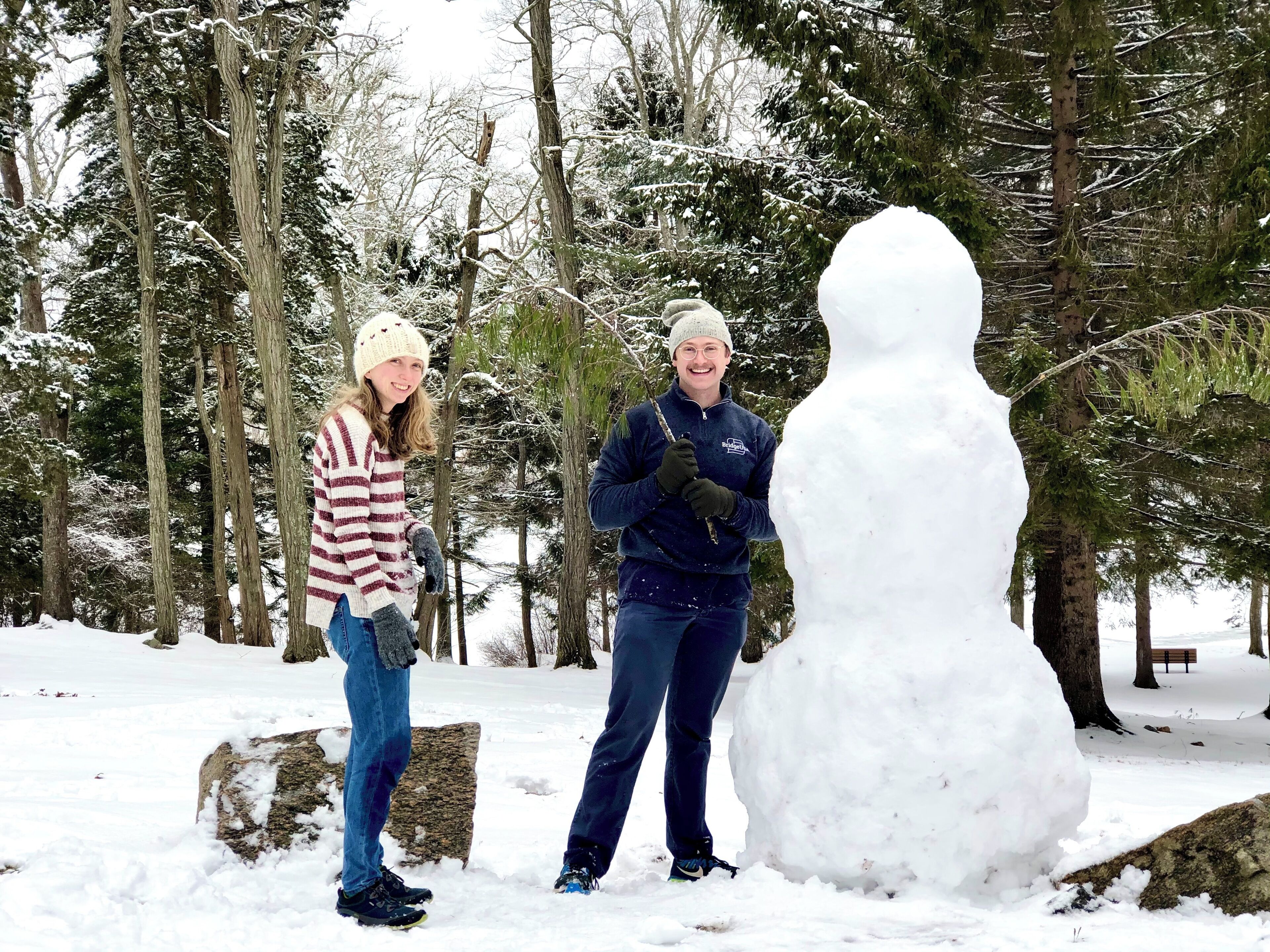 Two people standing in a snowy park with a large snowman.