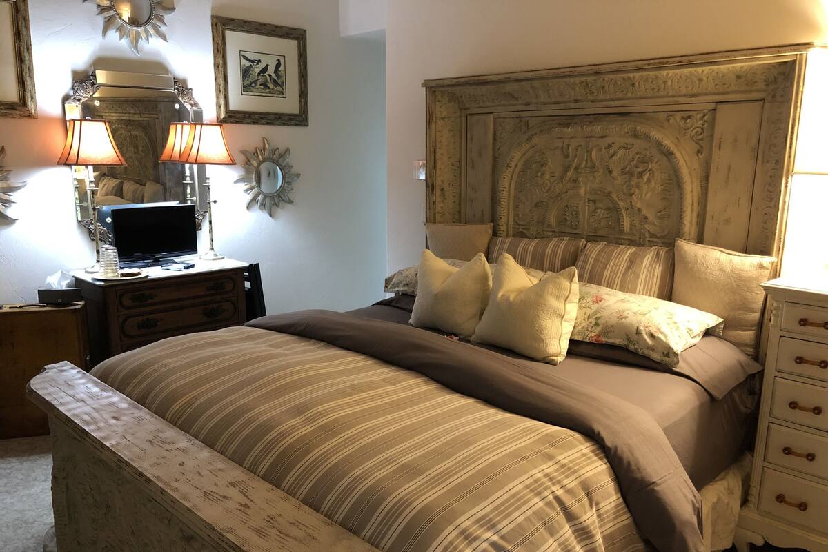 A bedroom with a large bed, a wooden nightstand, a dresser, and a lamp.