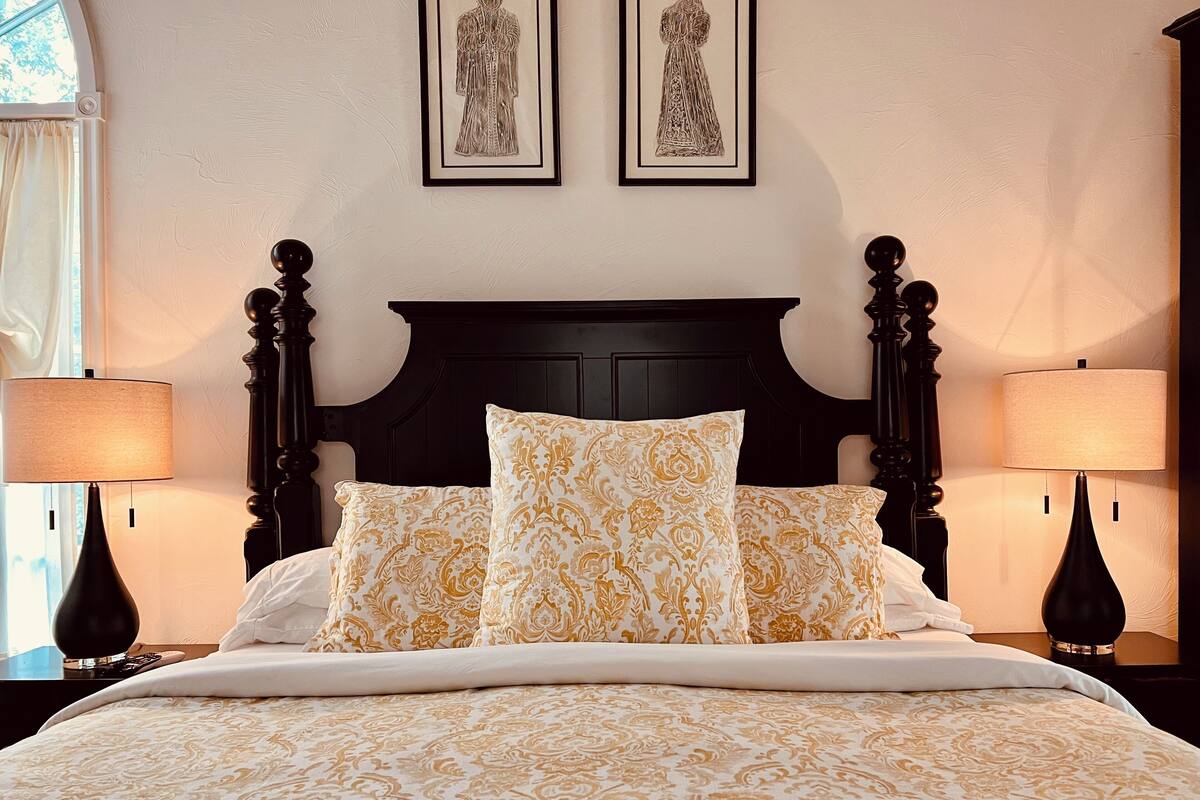 A neatly made bed with patterned bedding, two wall-mounted lamps, and two framed artworks above the bed.