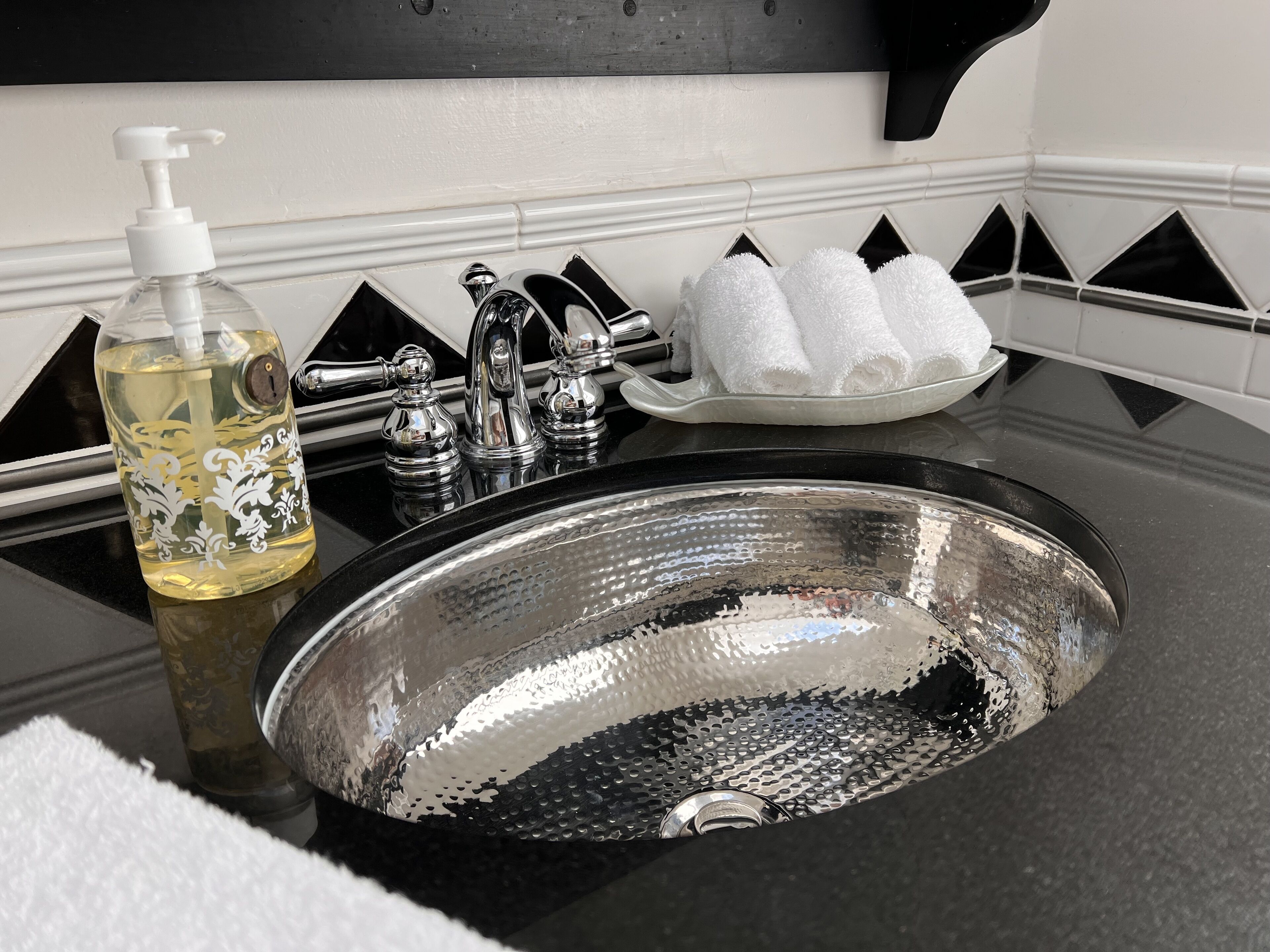 A bathroom sink with a decorative bottle, a soap dispenser, and a towel rack with folded towels.