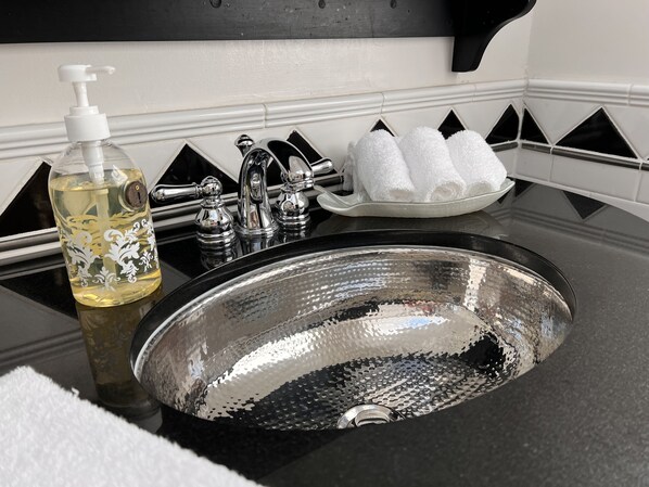 A bathroom sink with a decorative bottle, a soap dispenser, and a towel rack with folded towels. - Frederick William House (Falmouth)