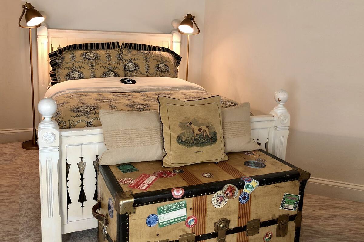 A bed with patterned bedding, a decorative pillow, and a suitcase with travel stickers.