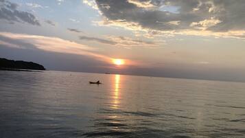 Mar tranquila con un bote y un barco distante, bajo un cielo parcialmente nublado con el sol poniéndose o saliendo.