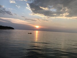 Mar tranquila con un bote y un barco distante, bajo un cielo parcialmente nublado con el sol poniéndose o saliendo.