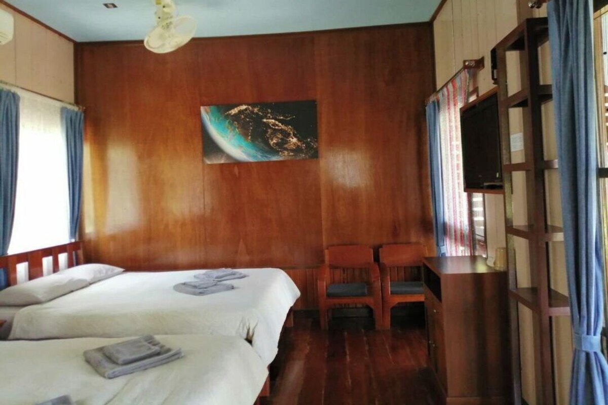 Une chambre avec deux lits, un mur en bois, un tableau, une télévision et une fenêtre avec des rideaux.