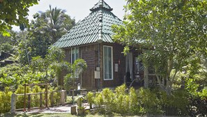 Un petit bâtiment en bois, surmonté d’un toit vert, entouré d’une végétation luxuriante et d’une clôture en bois.