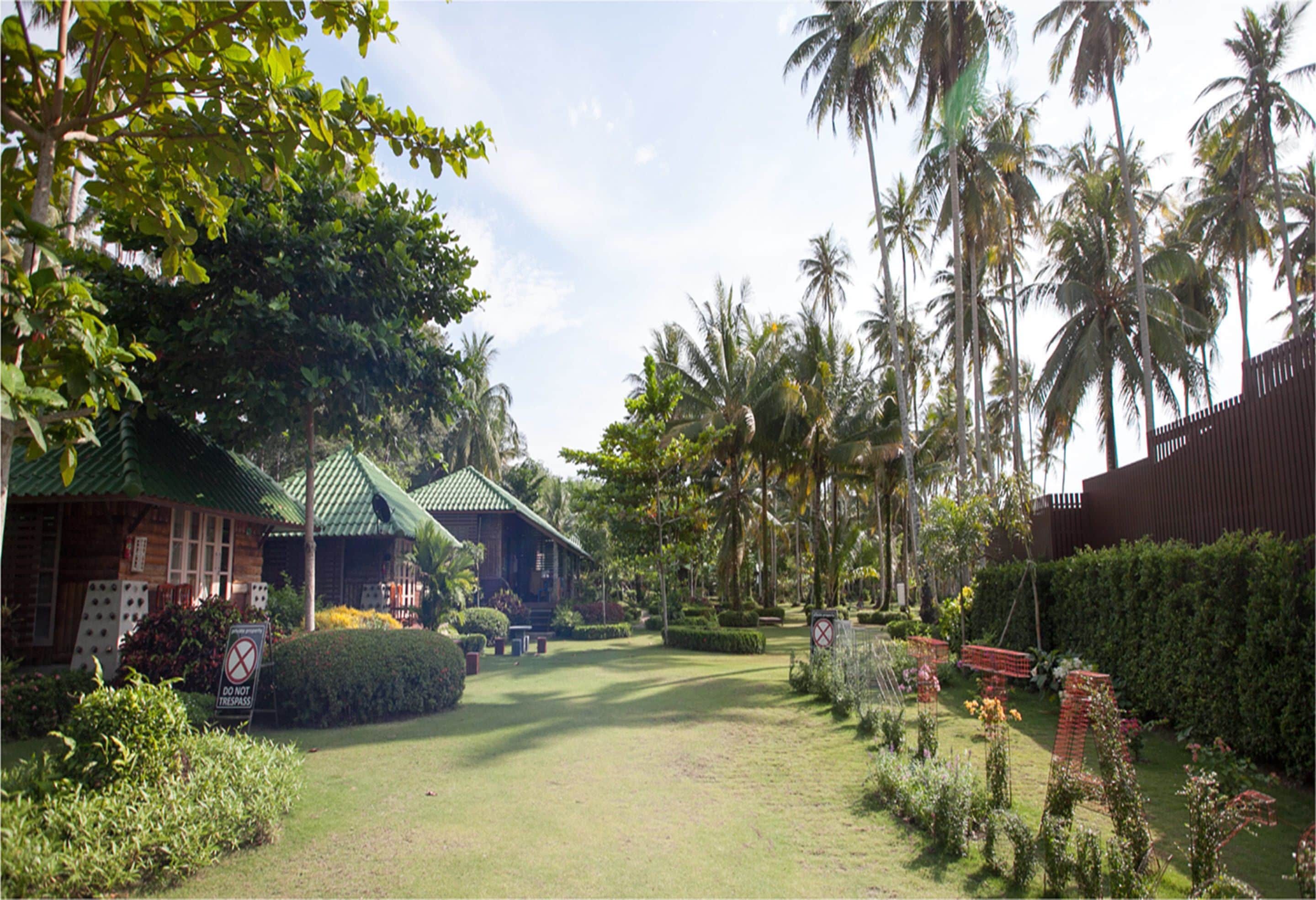 A tropical resort with a well-maintained lawn, palm trees, and a wooden building with a green roof.