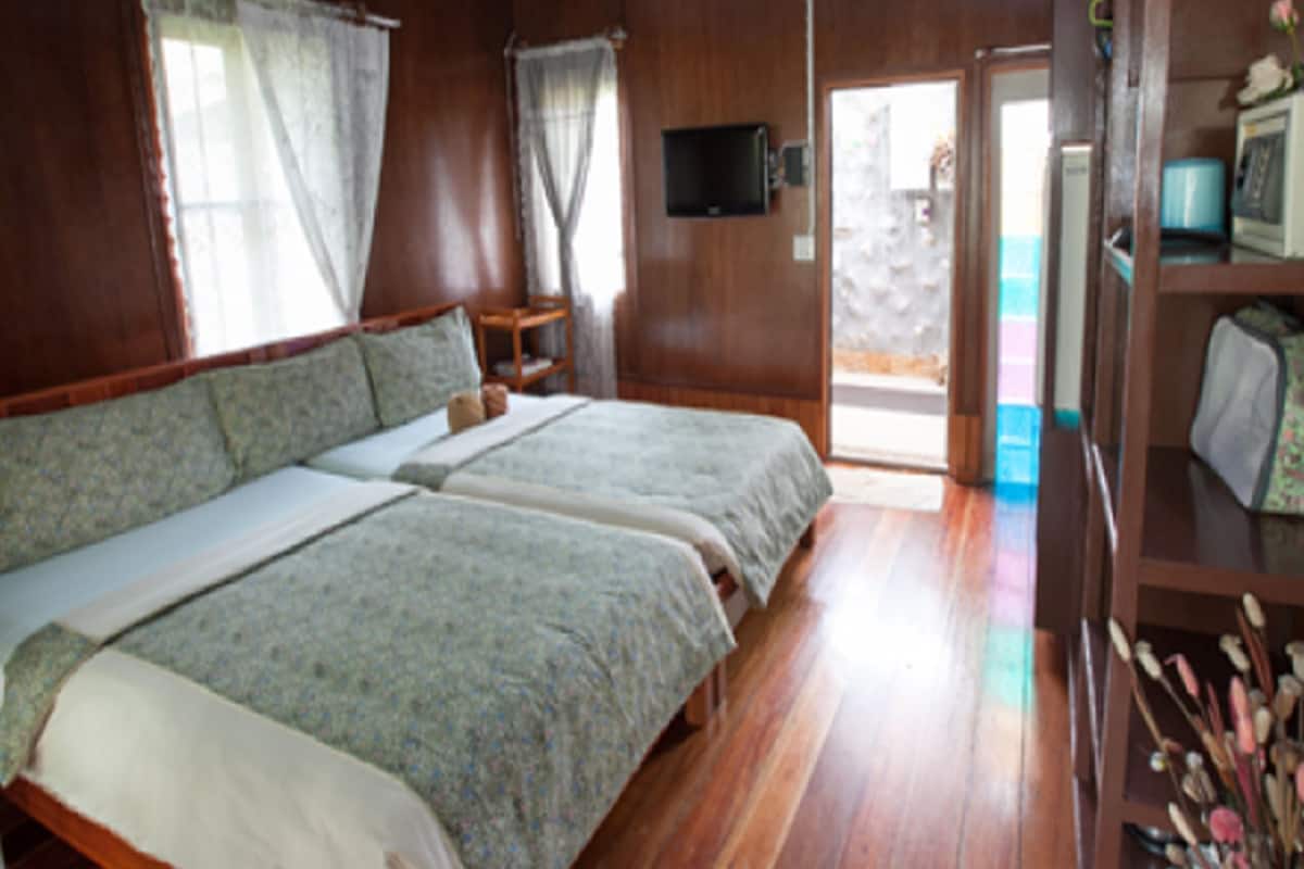 Ein Zimmer mit zwei Betten, Holzboden, einem an der Wand befestigten Fernseher und einem kleinen Tisch.