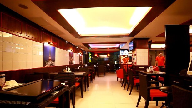 A restaurant with a long counter, booths, and tables. There are large windows along one wall, and a ceiling with recessed lighting. - Rayaan Oriental Guest House & Restaurant (Patong)