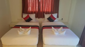 A hotel room with two beds, each with a white bedspread and red and black pillows. There are two white towels placed on the beds.