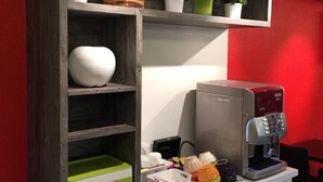 A kitchenette with a coffee machine, shelves with plants, and a colorful storage box. - Brit Hotel Rouen Sud / Val De Reuil (Val-de-Reuil)