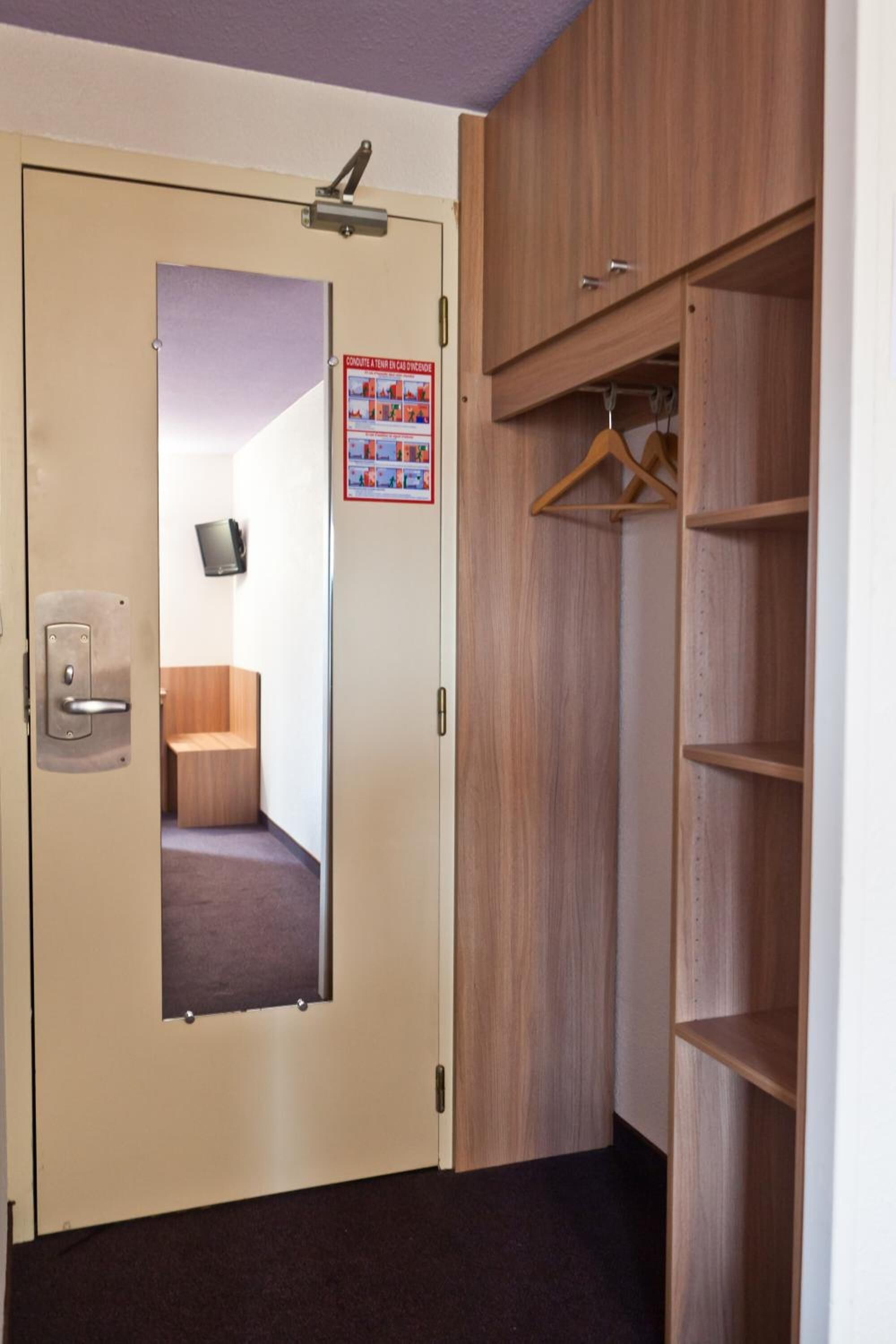 A room with a beige door, a wooden wardrobe with shelves, and a mirror.