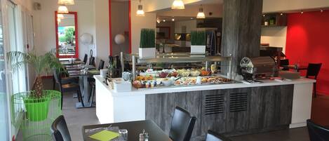 A modern restaurant with a buffet, black chairs, and a red accent wall.