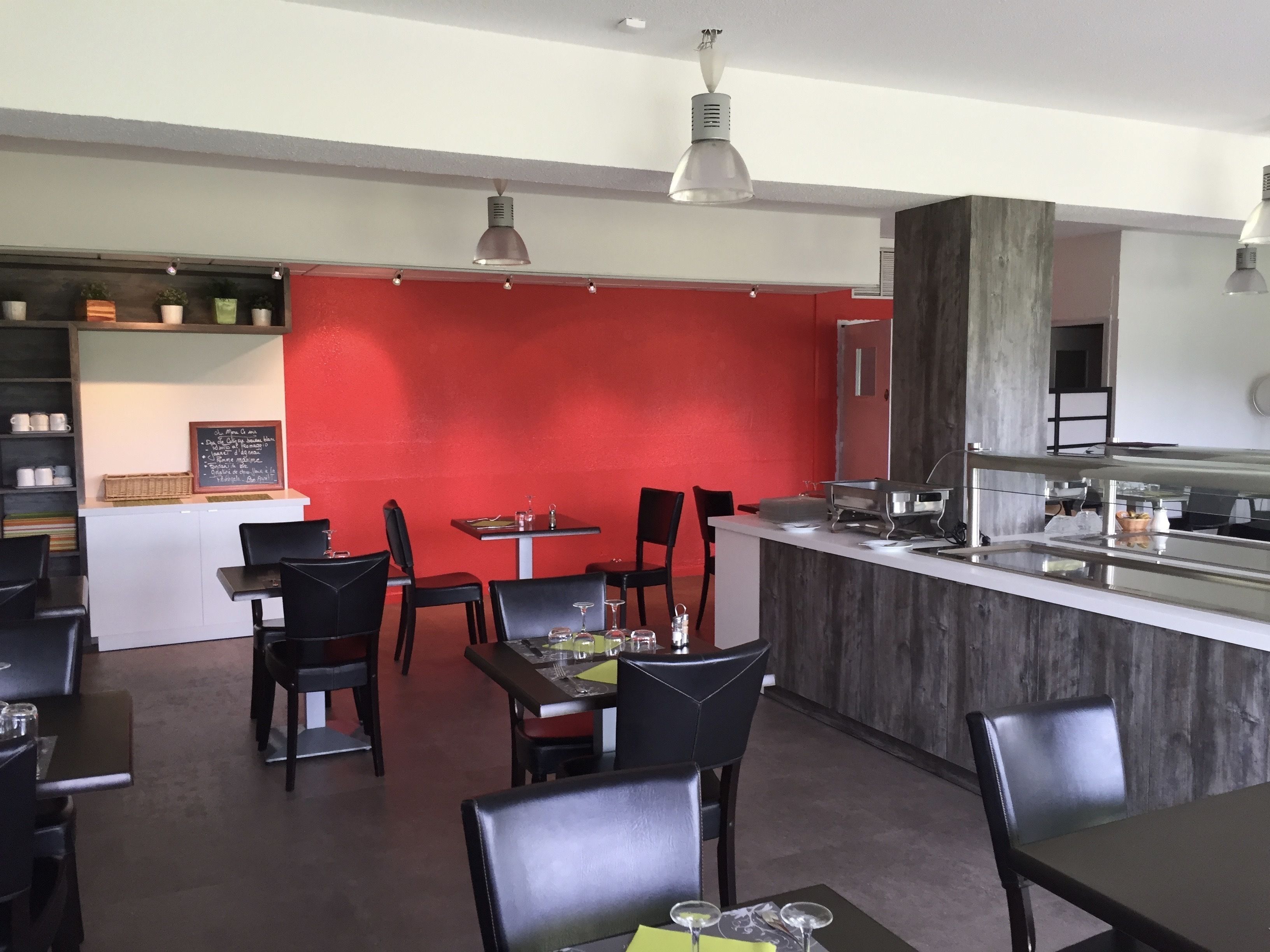 A restaurant with a red wall, black chairs, and a counter with a sink.