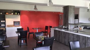 A restaurant with a red wall, black chairs, and a counter with a sink.