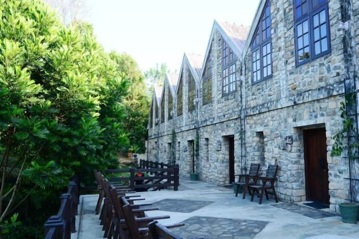 A stone building with multiple windows and doors, a paved courtyard, and wooden furniture.