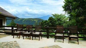 Un patio con sillas de madera y piso de piedra, con vista a un paisaje montañoso.