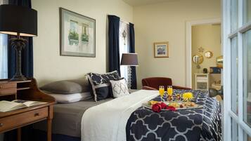 A neatly arranged hotel room with a bed, a desk, a chair, and a dining table set with breakfast.