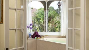 A bathroom with a bathtub, a window with a view of greenery, and a chandelier.