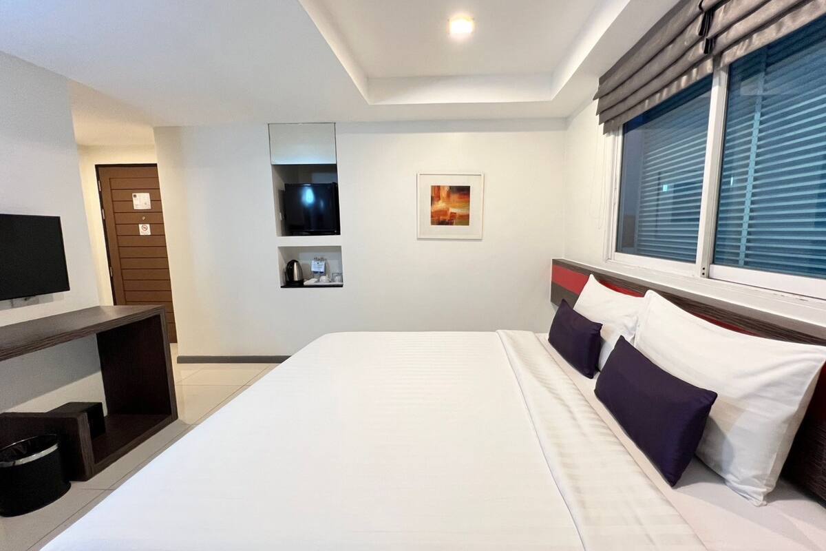 A modern hotel room with a large bed, a flat-screen TV, a coffee machine, and a painting on the wall.