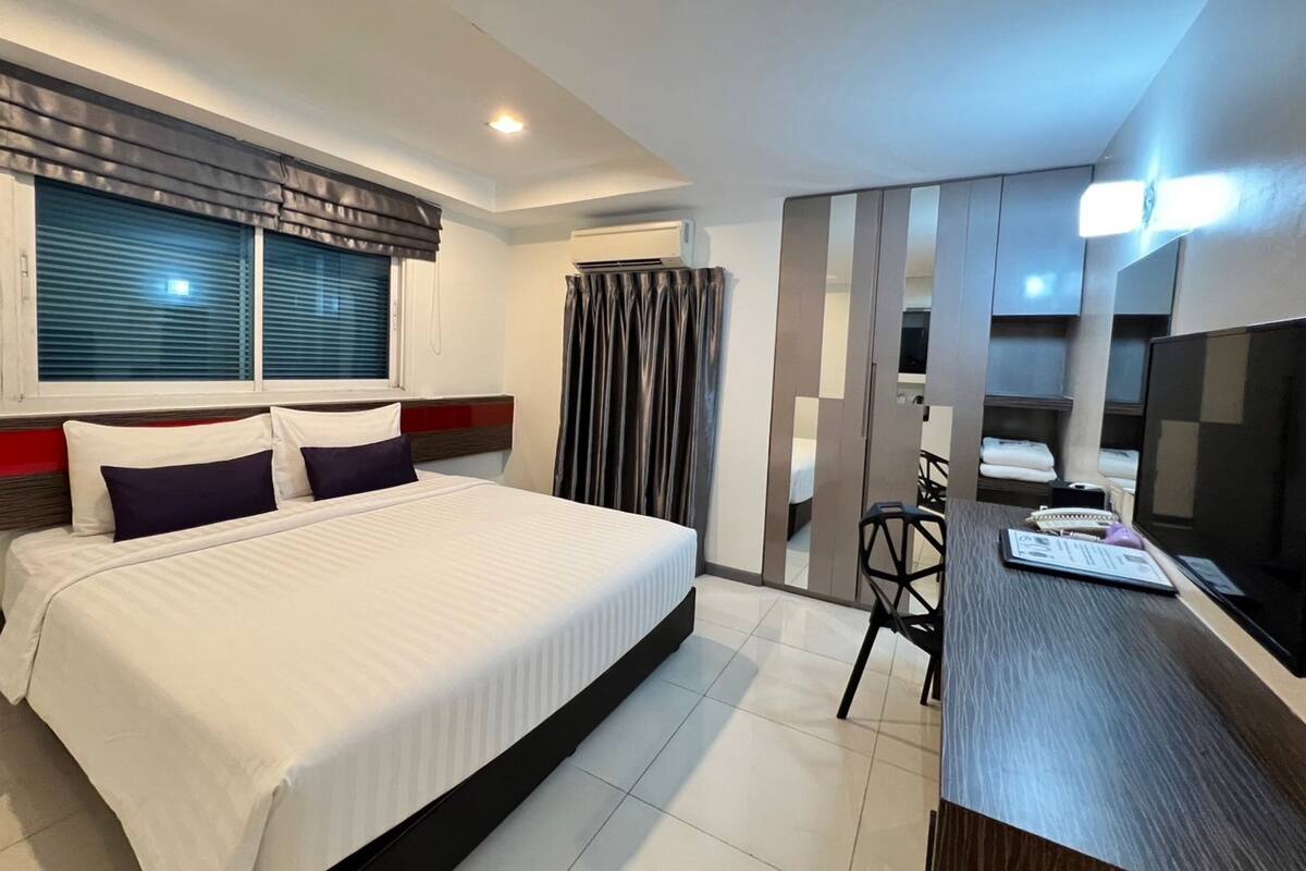 A hotel room with a bed, a desk, a chair, a TV, and a window with blinds.