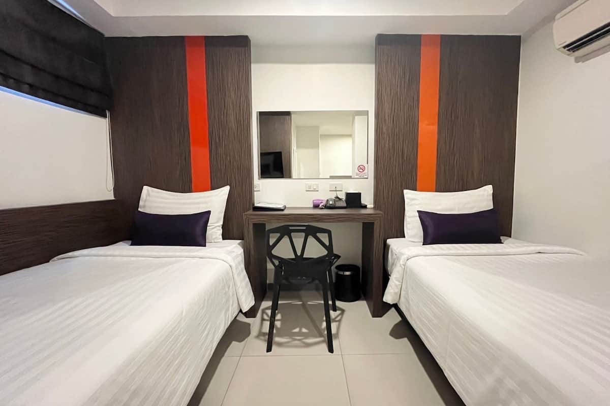 A hotel room with two single beds, a desk with a chair, a mirror, and an air conditioning unit.