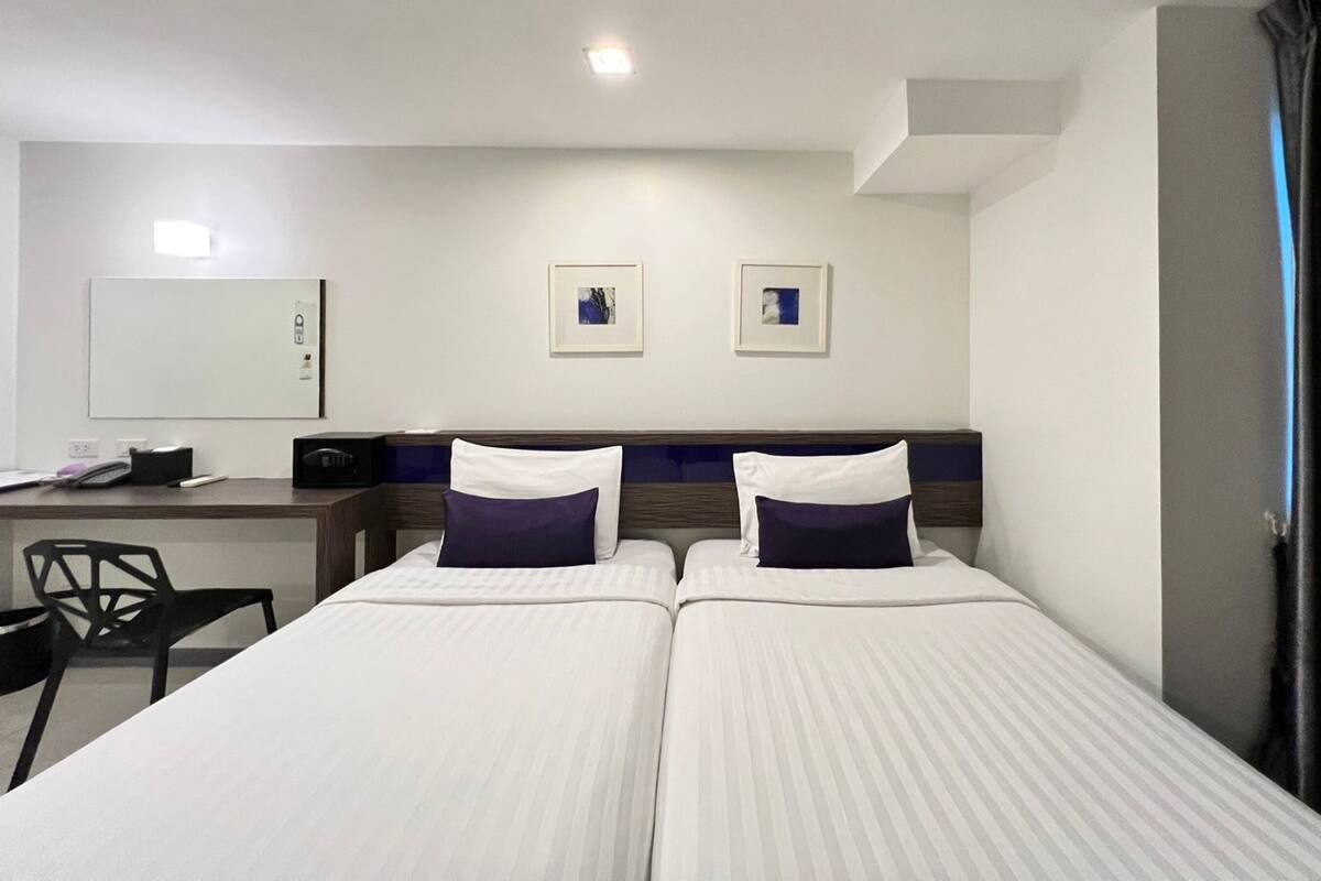 A hotel room with two beds, a desk, a chair, and a large mirror.