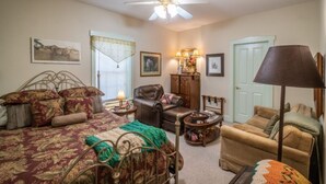 A cozy bedroom with a bed, a chair, a sofa, a lamp, and a ceiling fan. - Stone Haus Bed & Breakfast (Hermann)