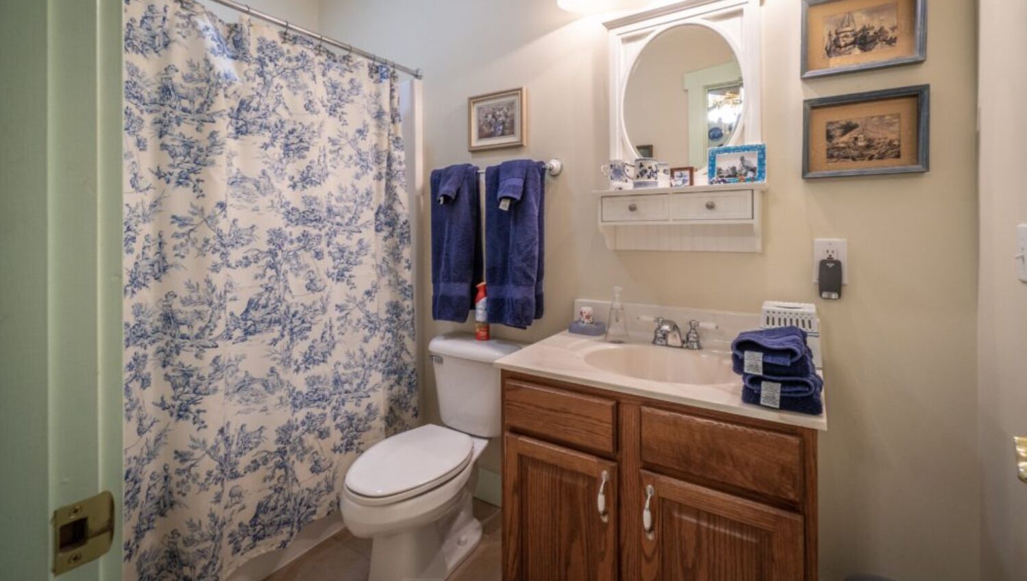 A bathroom with a toilet, a sink, and a shower curtain. There are towels hanging on the wall and a mirror above the sink.