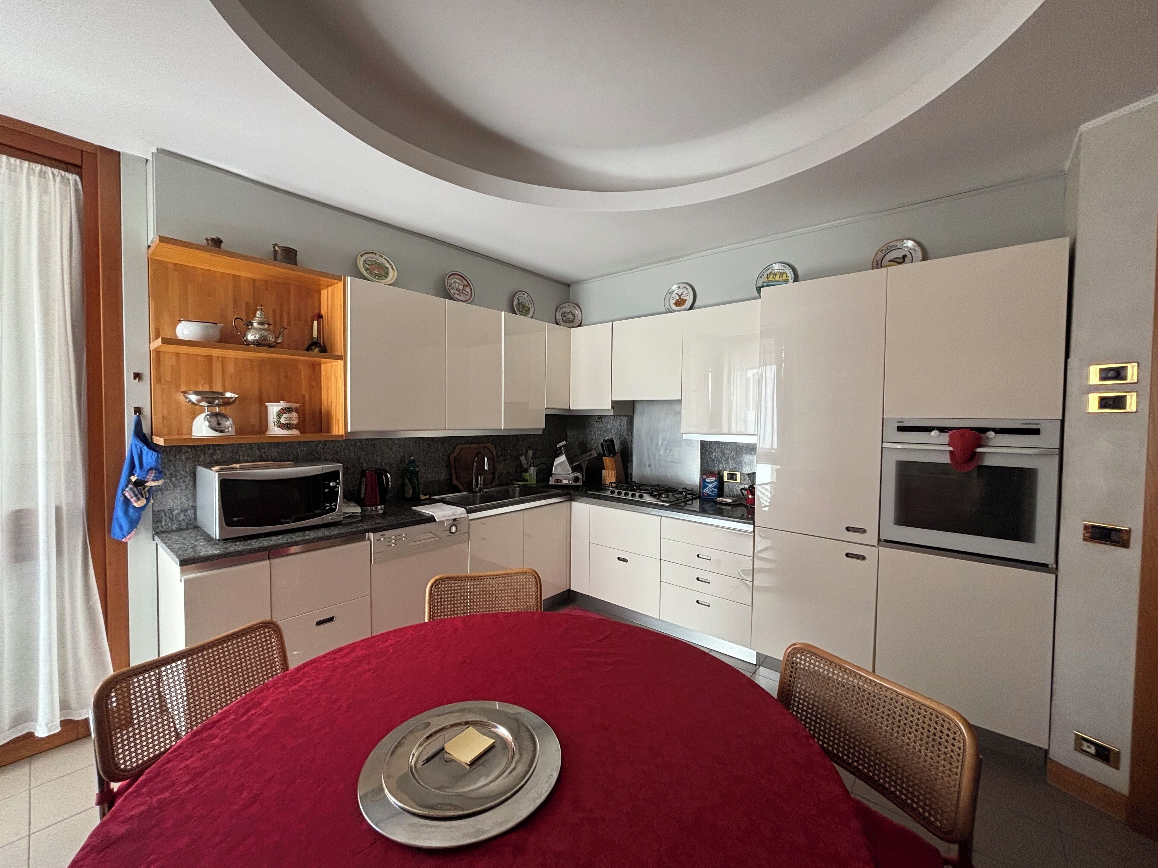 Cocina compacta con armarios blancos, microondas, estufa y una mesa de comedor roja para dos.